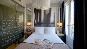 A hotel room with a large bed, a bedside table with a lamp, a mirror, and a view of the outside. - Hôtel Littéraire le Swann, BW Premier Collection (Paris)