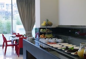 A buffet with various food items and a dining area with red chairs and a table.