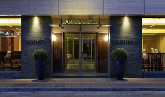 The exterior of the Samaria Hotel with a modern design, featuring a glass entrance and two potted plants at the entrance.
