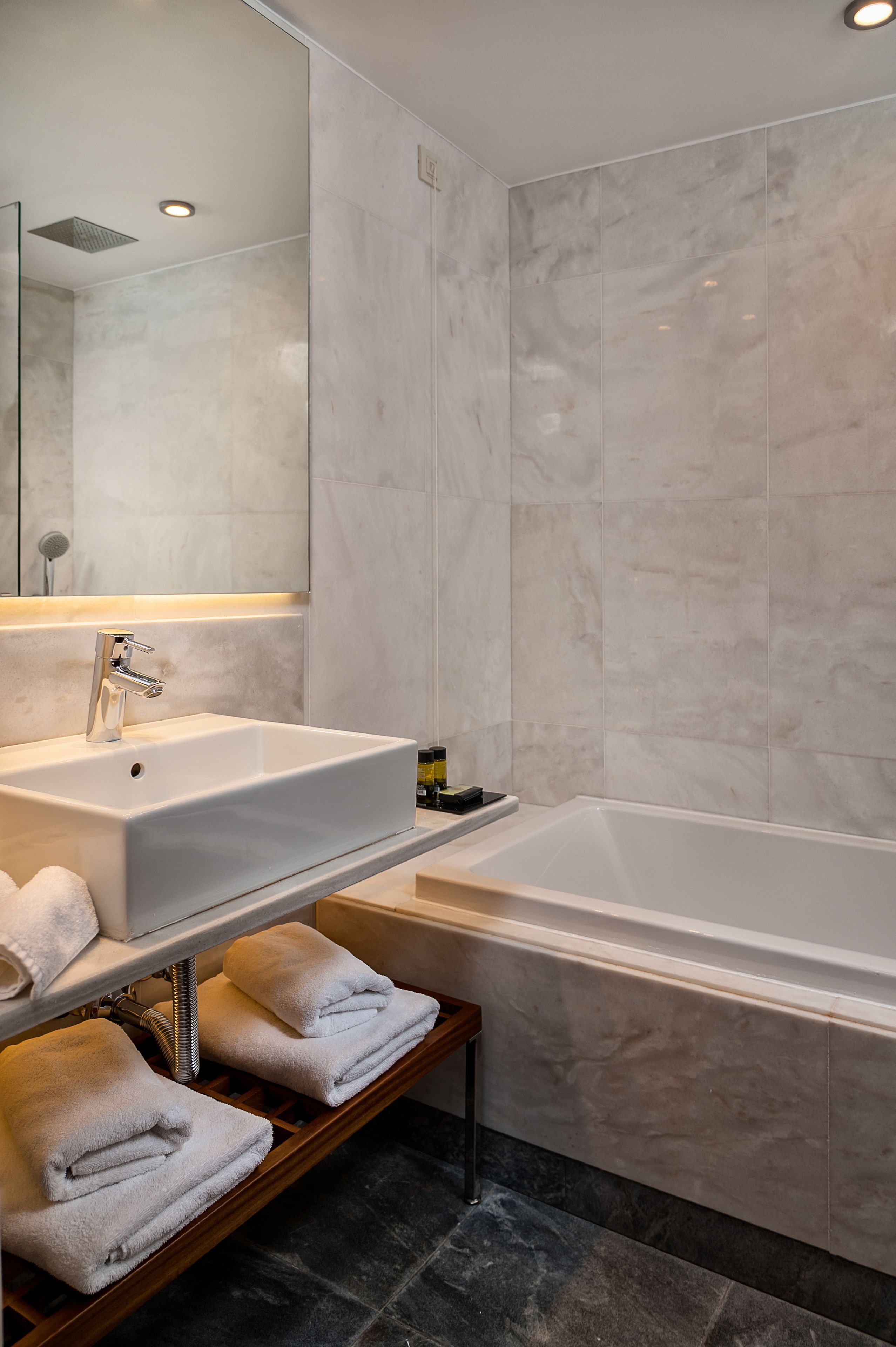 A modern bathroom with a large mirror, a white sink, a bathtub, and neatly folded towels on a shelf.