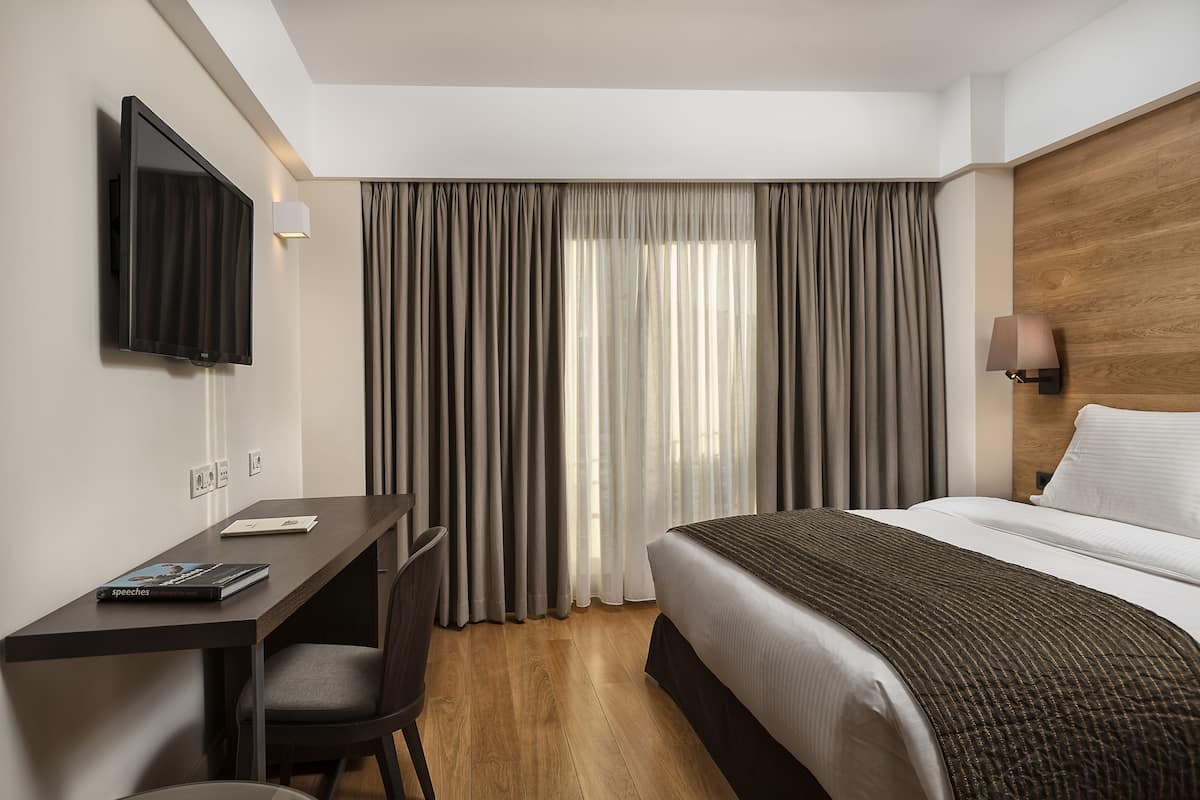 Une chambre d’hôtel avec un lit, un bureau, une chaise, une télévision et des rideaux.