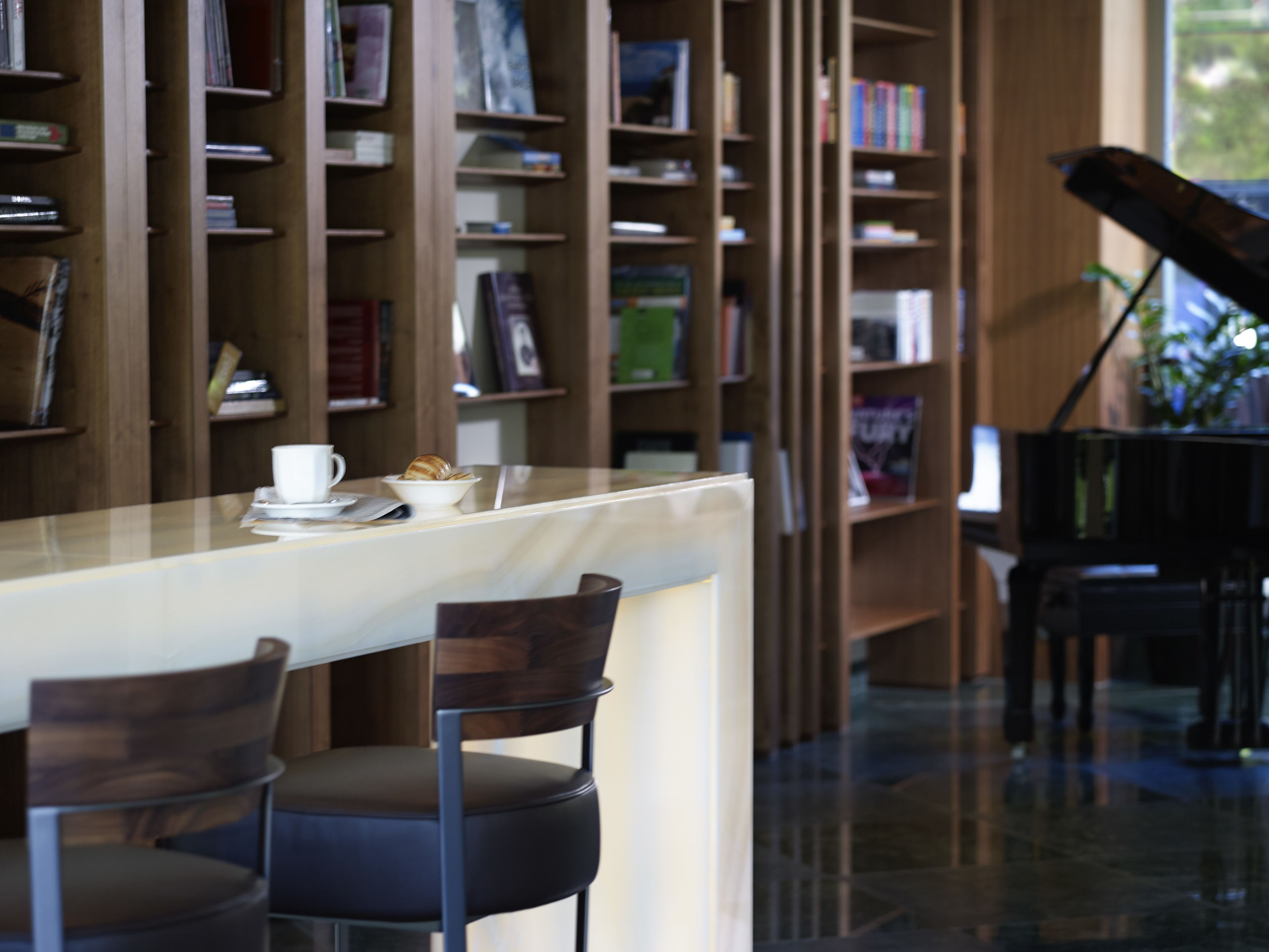 A library with bookshelves, a piano, and a table with chairs.