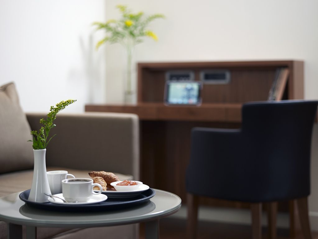 A hotel reception area with a reception desk, a vase with flowers, a tray with a croissant, and a cup of coffee.