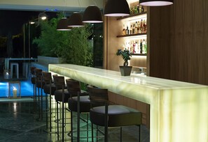 A bar area with a marble counter, bar stools, pendant lighting, and a potted plant.