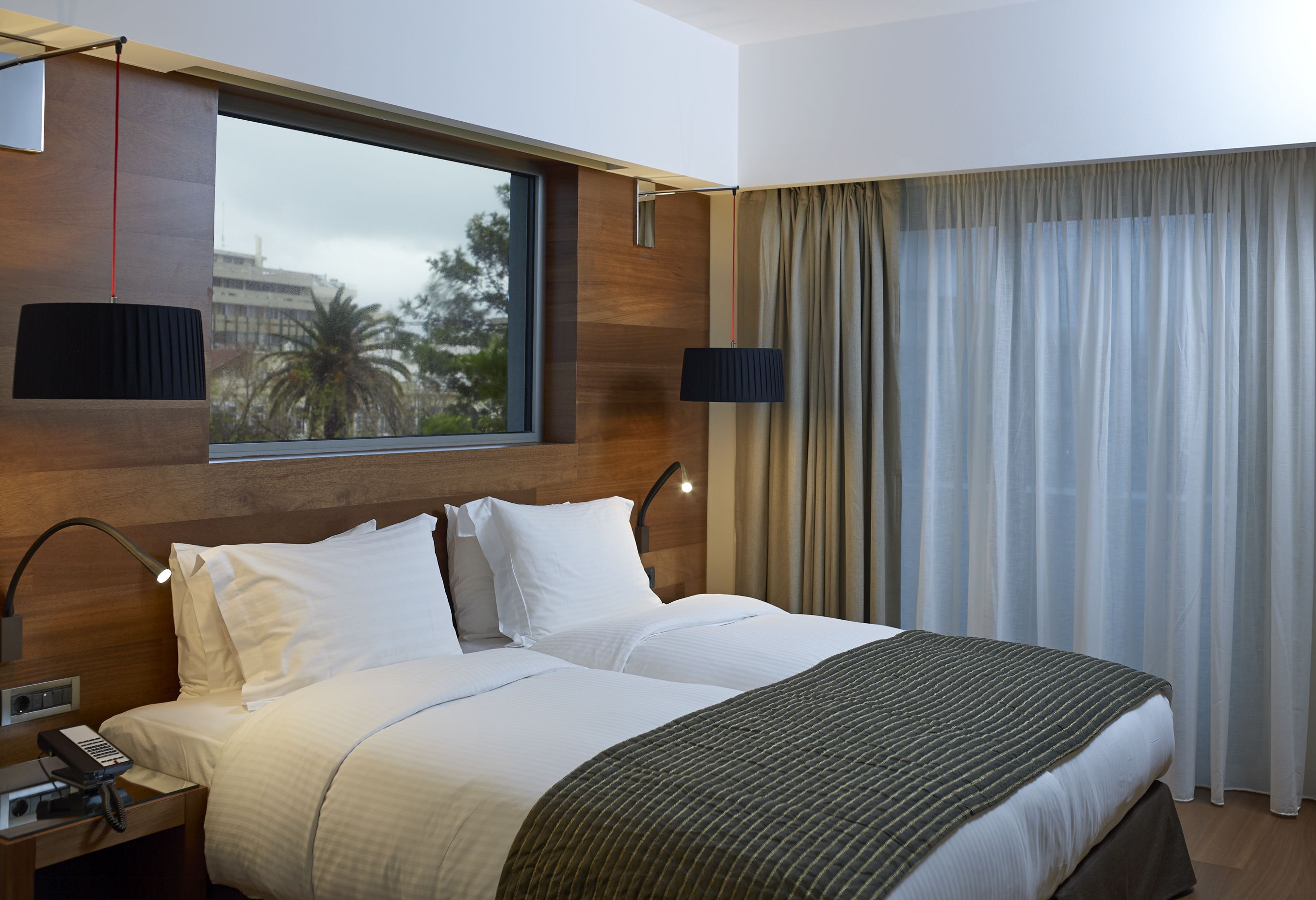 Une chambre d’hôtel avec un grand lit, une table de chevet avec une lampe, un téléphone et une fenêtre avec des rideaux.
