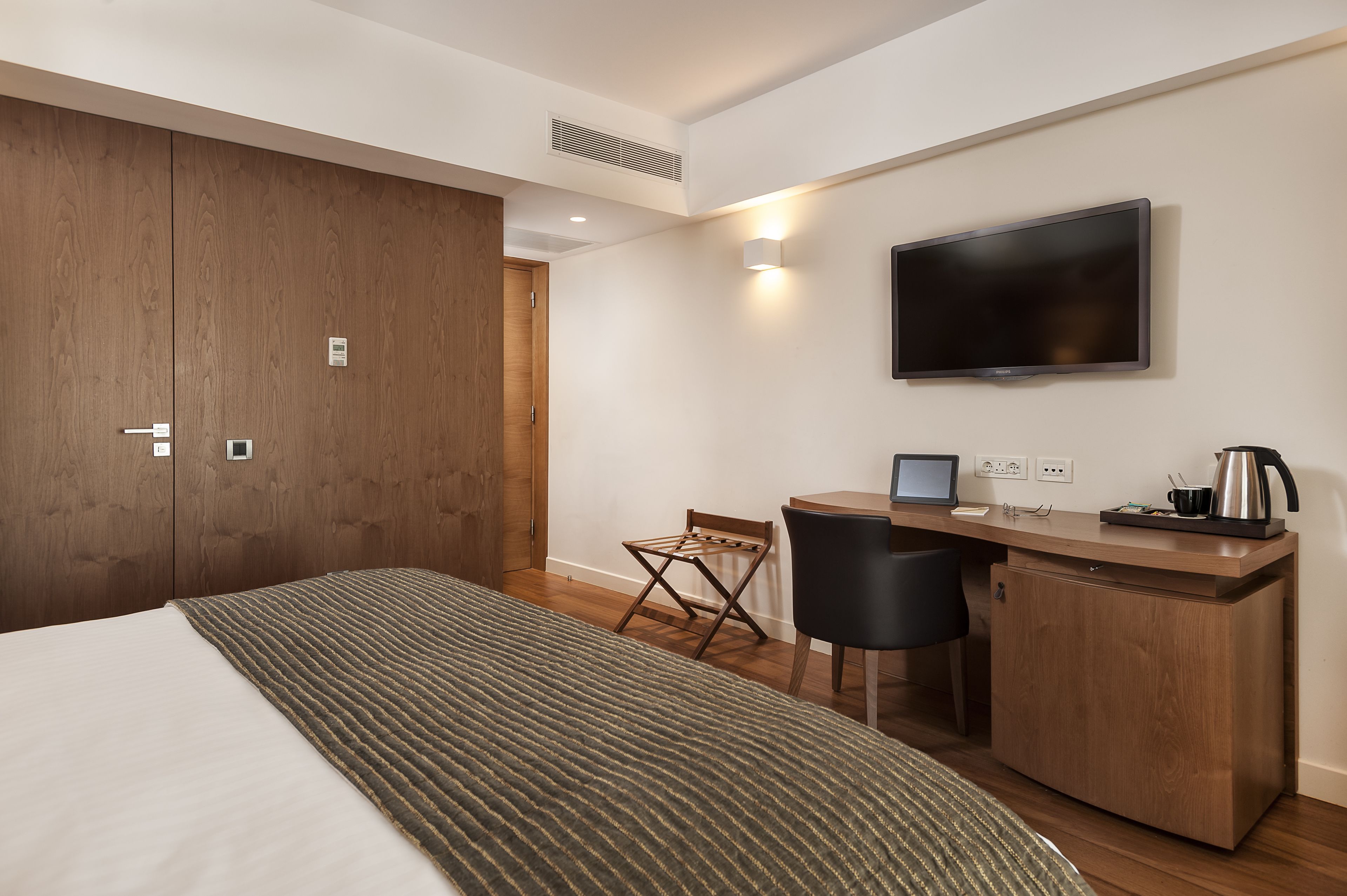 A hotel room with a bed, a desk with a computer, a TV, and a small kitchenette.