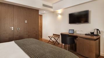 A hotel room with a bed, a desk with a computer, a TV, and a small kitchenette.