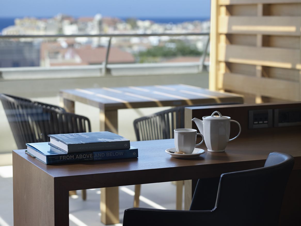 Un balcón con una mesa, sillas, una tetera blanca, una taza y dos libros titulados "From Above and Below".
