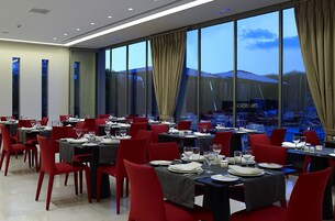 A restaurant with tables set for dining, large windows, and red chairs.