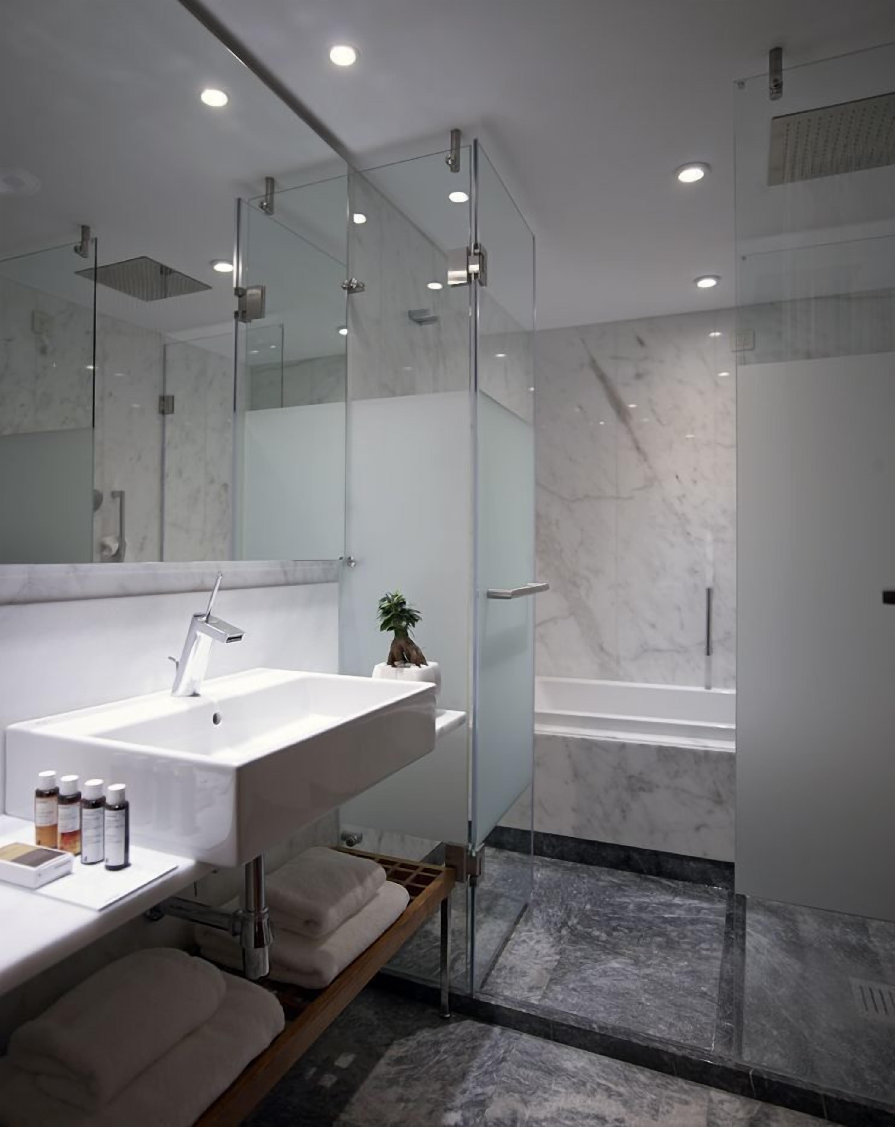 A modern bathroom with a large white sink, a glass shower enclosure, and a marble-tiled floor.