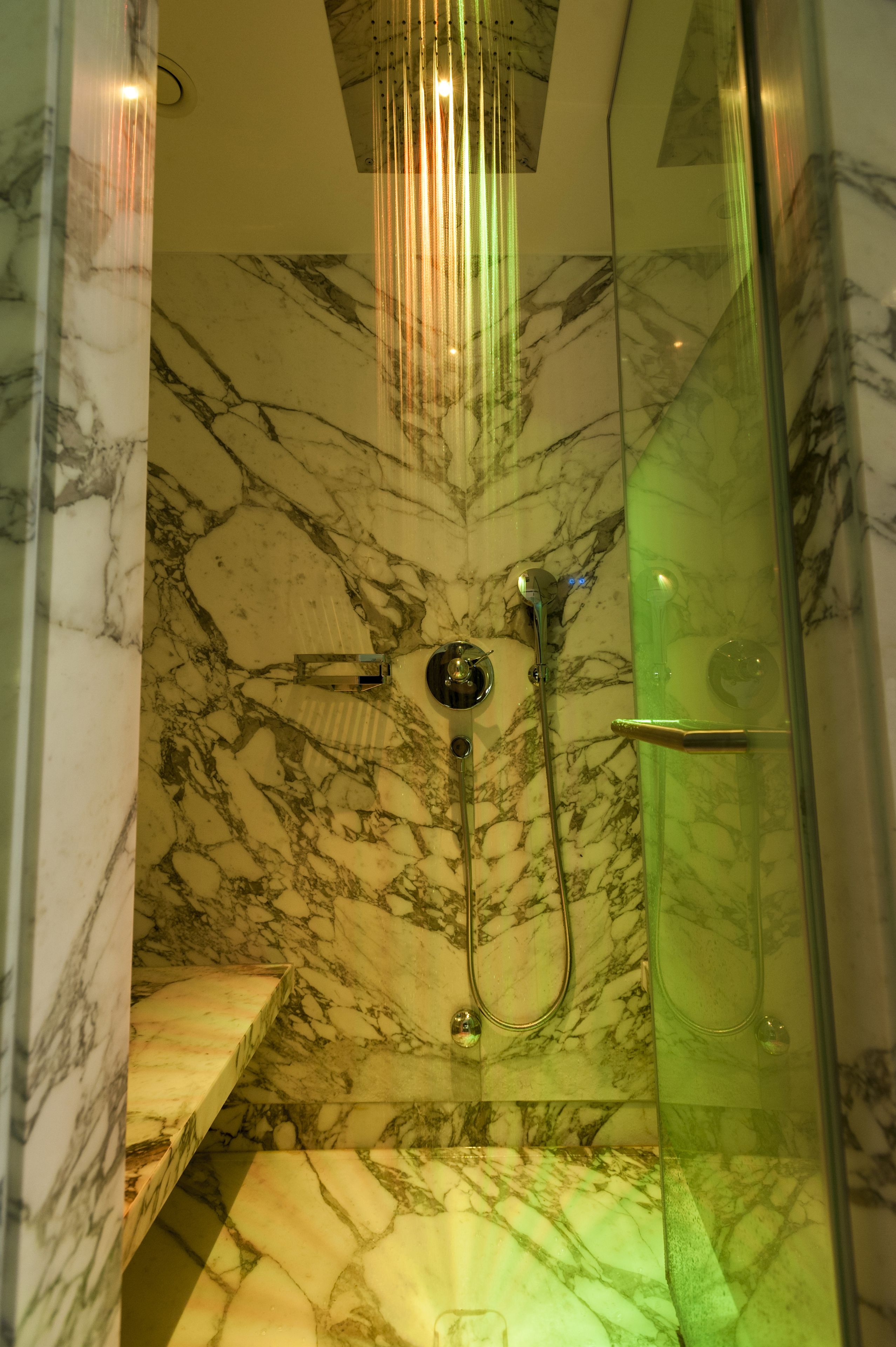 A bathroom with a marble wall, a glass shower enclosure, and a marble sink.
