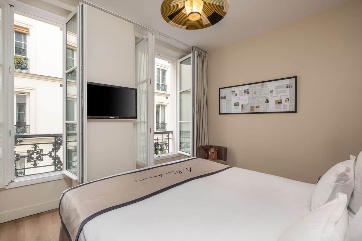 A hotel room with a bed, a TV mounted on the wall, a framed informational poster, and a view of the outside balcony.