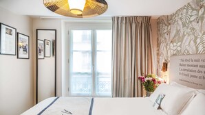 A hotel room with a bed, a large window with curtains, a wall-mounted light fixture, and framed pictures on the wall. - Hôtel Littéraire Arthur Rimbaud, BW Signature Collection (Paris)