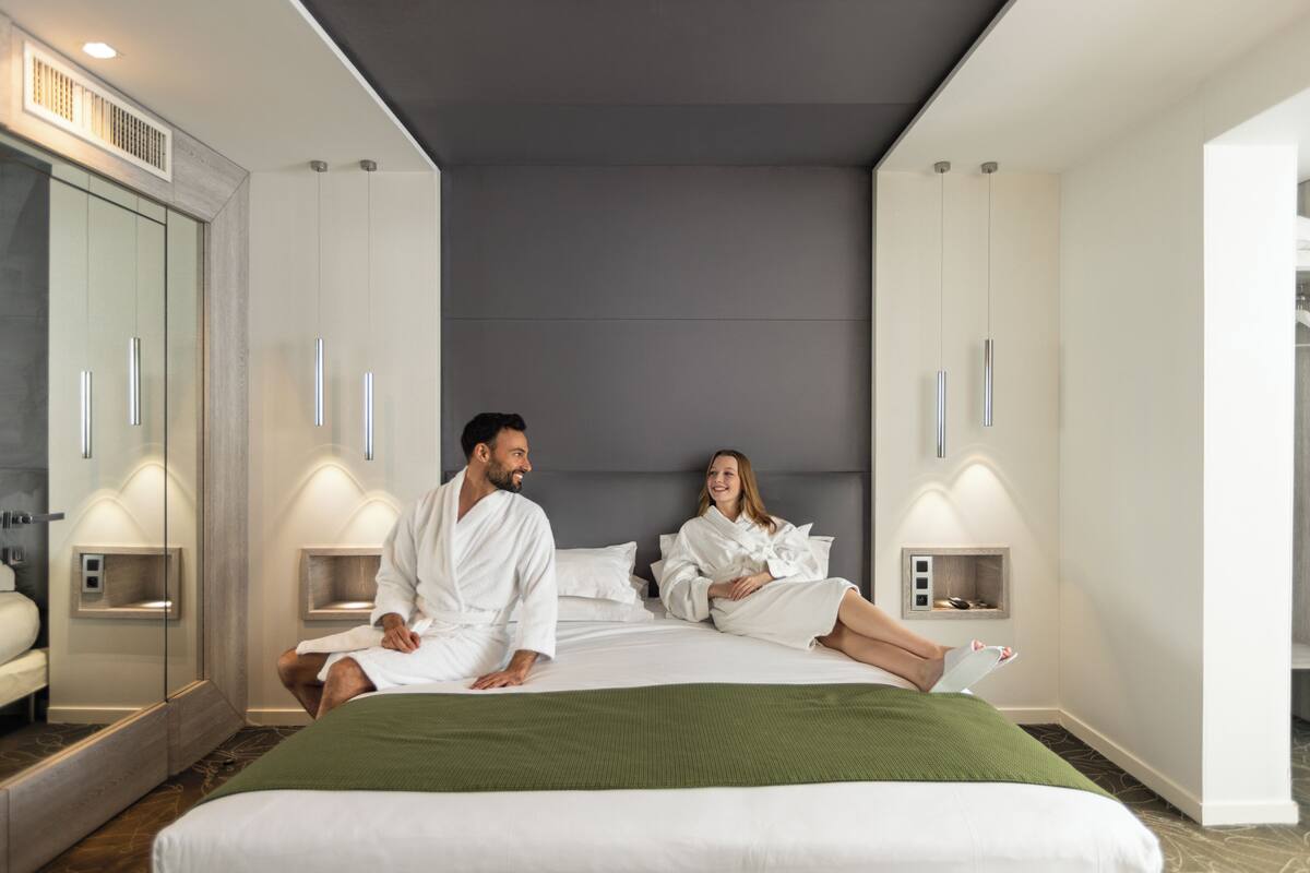 Una habitación de hotel moderna con una cama grande, dos mesitas de noche, un espejo y un armario.