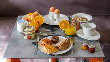 Una mesa de desayuno con huevos, gajos de naranja, un vaso de jugo de naranja, un frasco de mermelada, un muffin y un croissant.