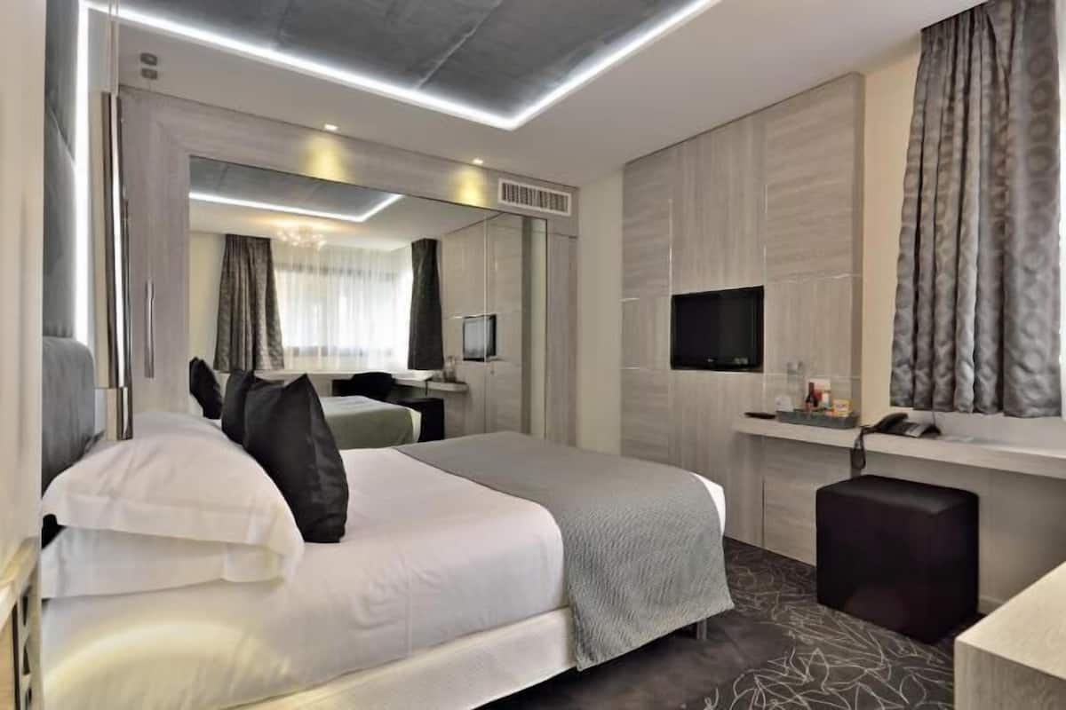 A modern hotel room with a bed, a desk, a TV, and a large mirror.