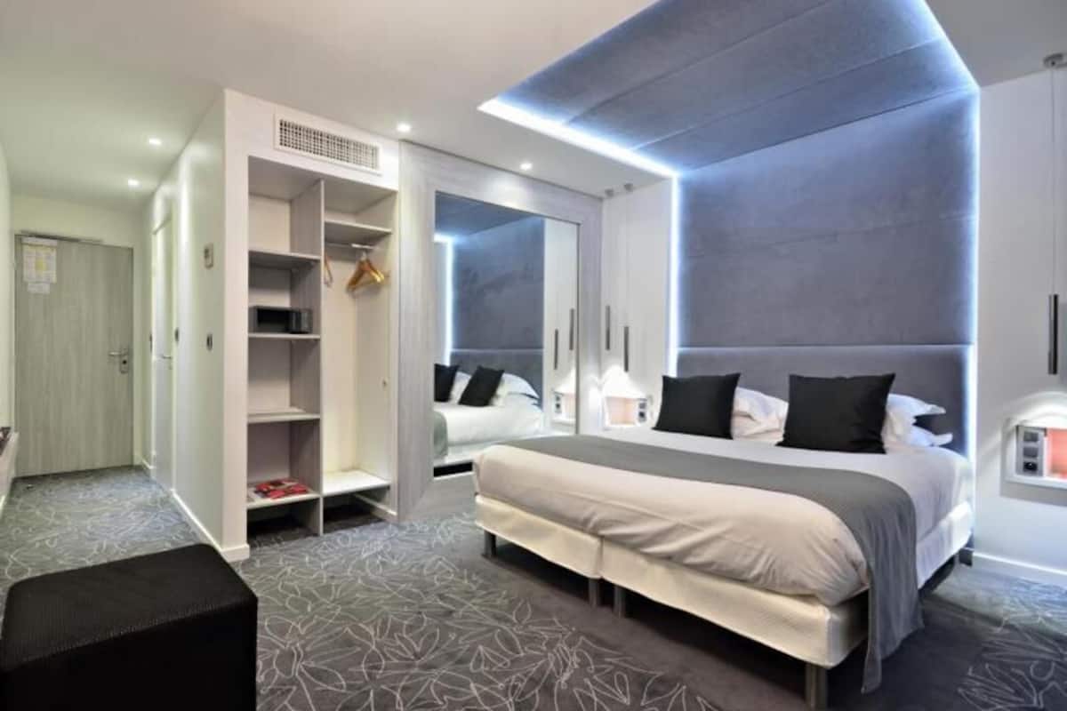 A modern hotel room with a large bed, built-in wardrobe, and a seating area.