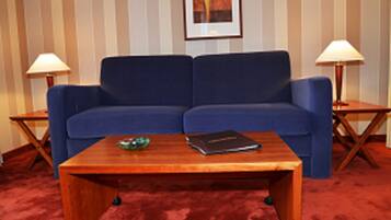 Un sofá azul frente a una pared a rayas, con dos mesitas auxiliares y una mesa de centro de madera en primer plano.