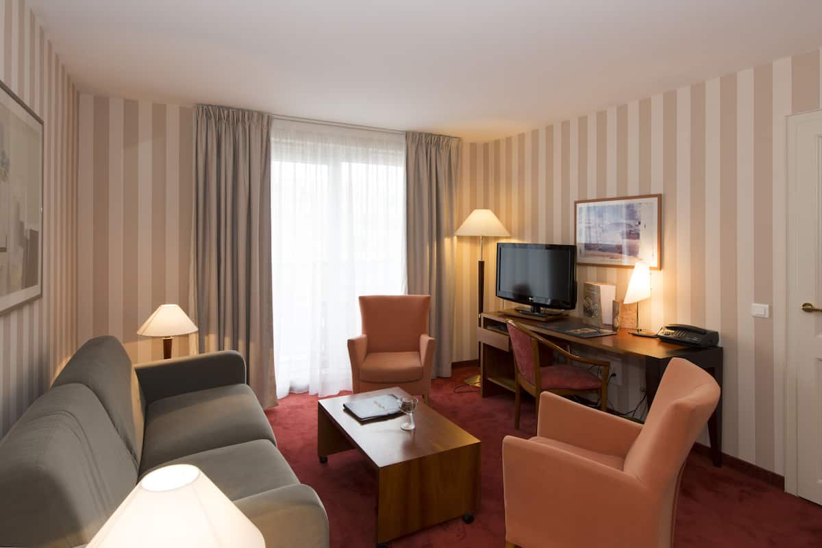 Quarto de hotel com parede listrada, um sofá, uma escrivaninha com computador, uma televisão e duas cadeiras.