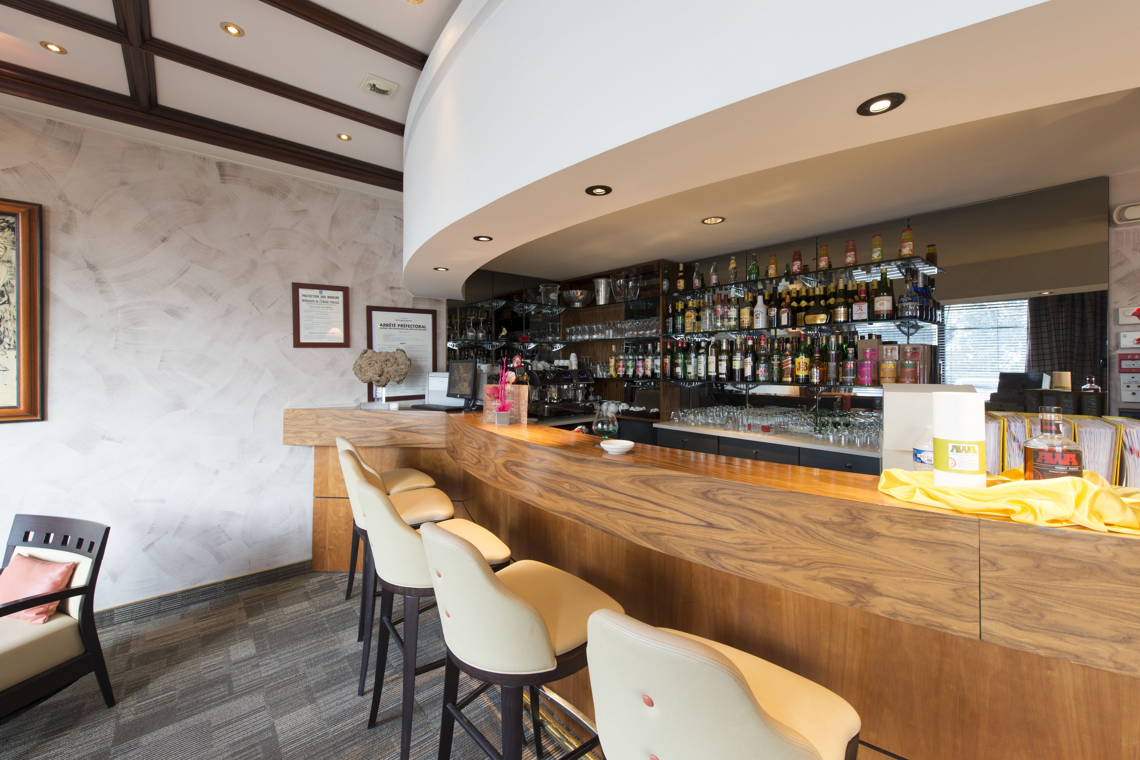 Una zona de bar con una barra curva, varios taburetes y una estantería bien surtida con diferentes botellas y copas.