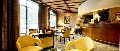 A hotel lobby with yellow chairs, a reception desk, and a large window providing a view of the city.