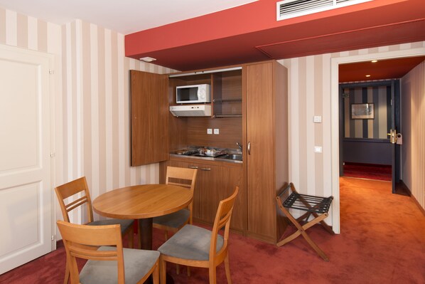 A compact kitchen with a microwave, stove, and wooden cabinets. There is a dining table with chairs and a small seating area with a bench.