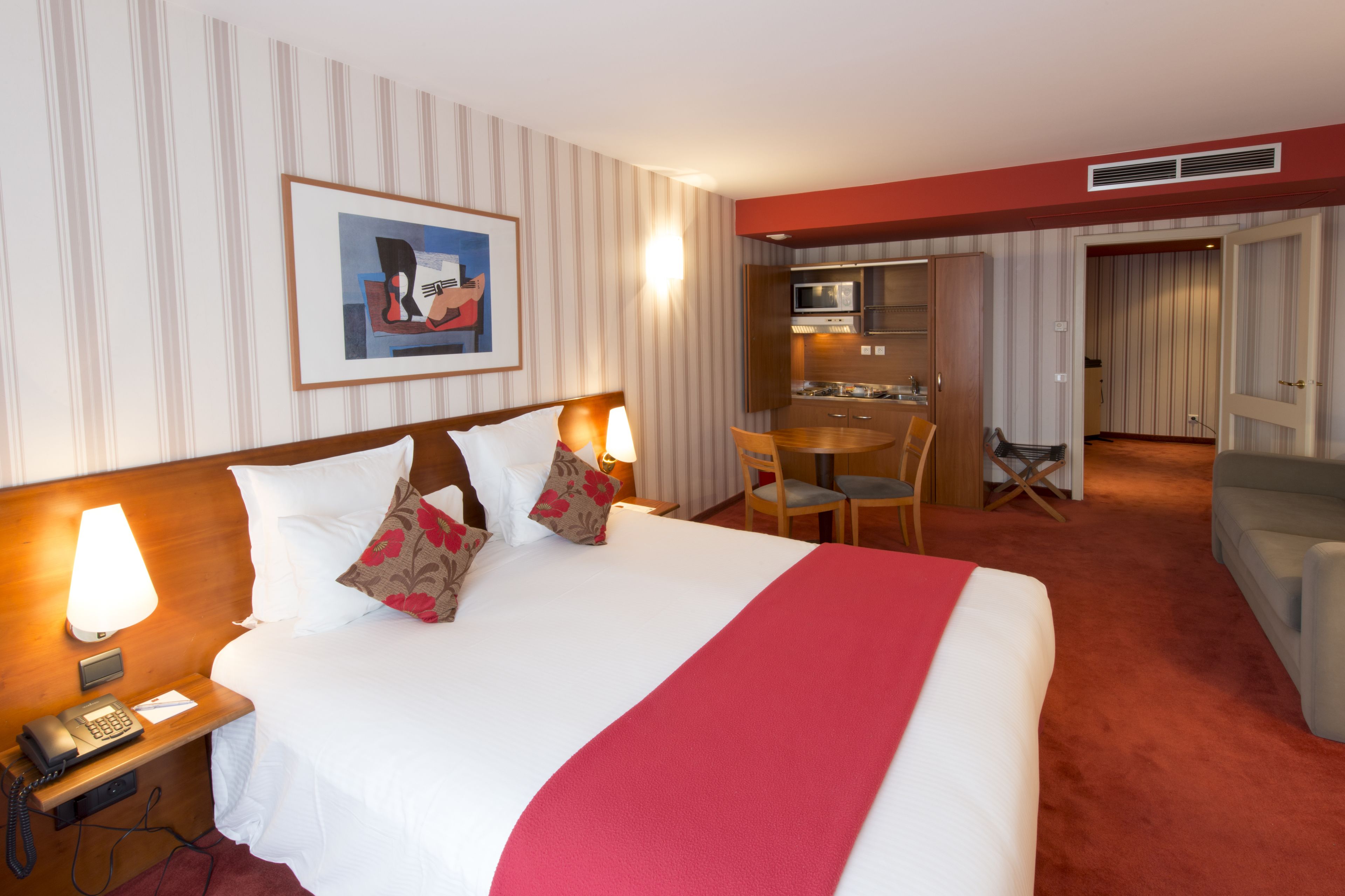 A hotel room with a bed, bedside lamp, telephone, and a painting on the wall.