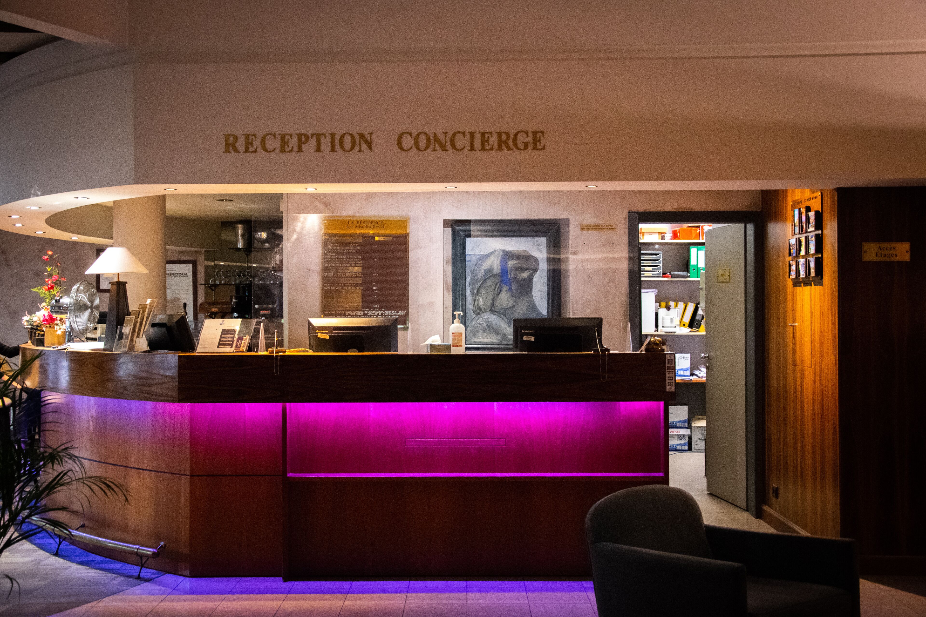 Un comptoir d’accueil avec une pancarte indiquant « RÉCEPTION/CONCIERGE » et un portrait encadré au-dessus.
