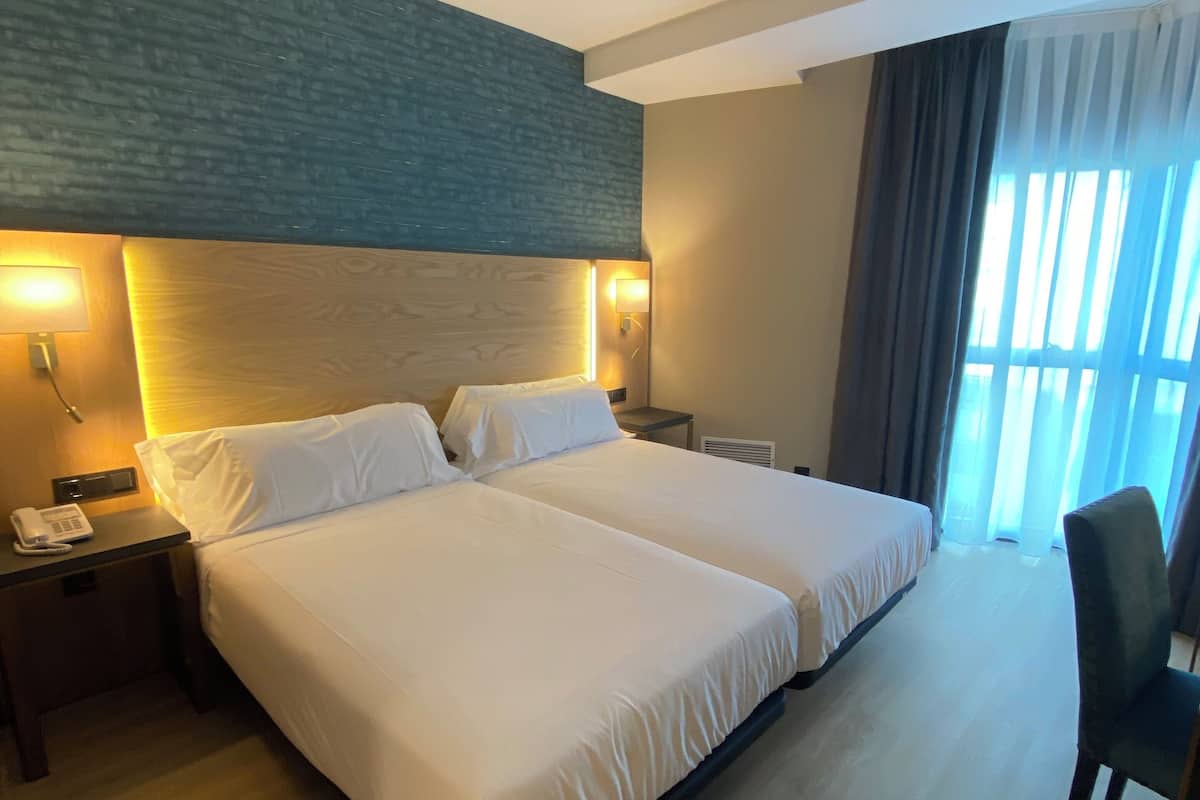A hotel room with a large bed, two bedside tables, a chair, and a window with curtains.