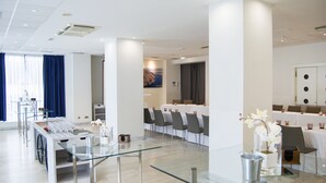 Un salón de conferencias moderno en un hotel, con mesas de vidrio, sillas y un gran ventanal con cortinas azules.