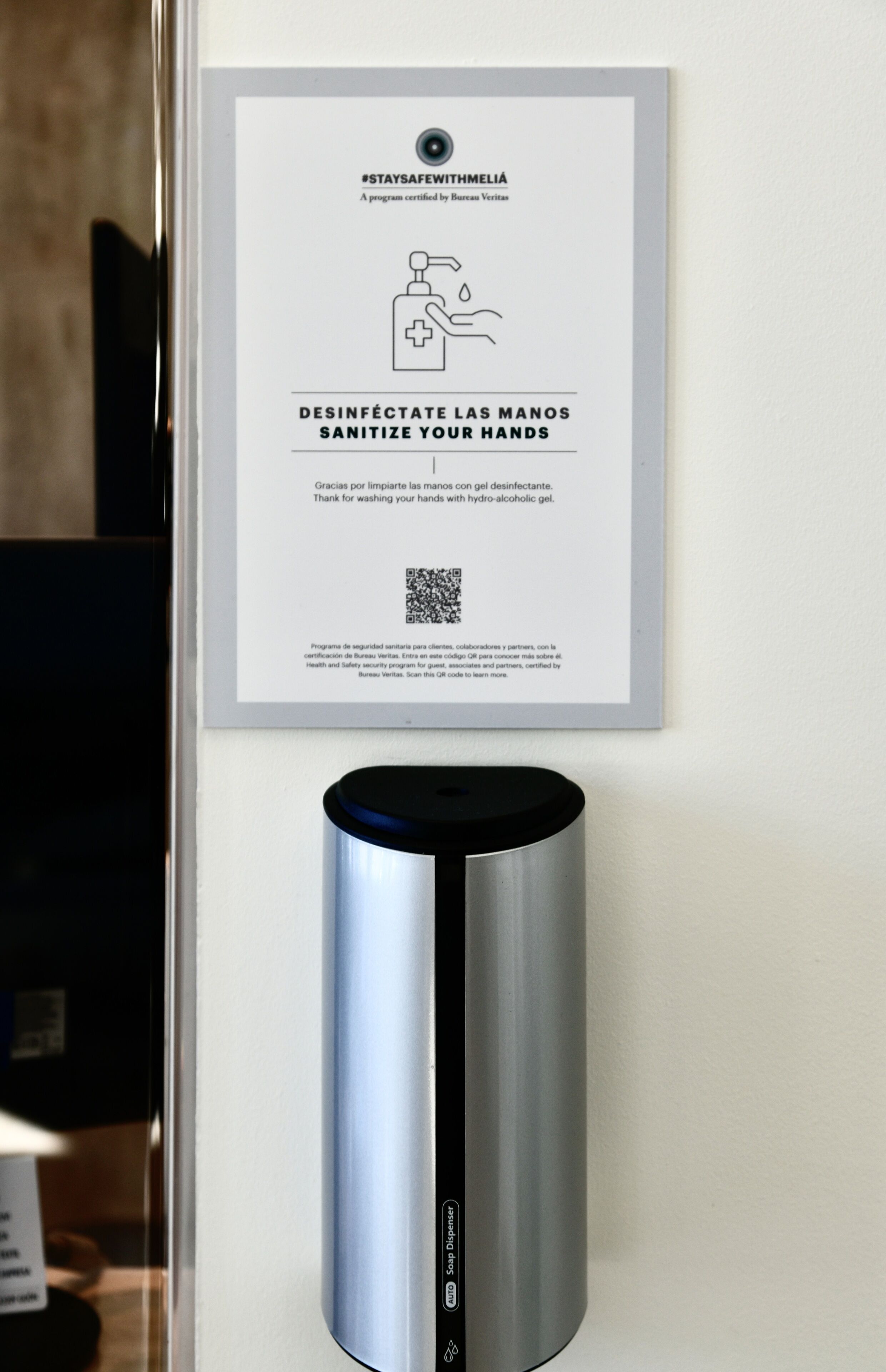 Un dispensador de gel antibacterial fijado a una pared, con un cartel encima.