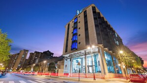 Un edificio moderno con fachada de vidrio, una entrada destacada y un estacionamiento al frente.