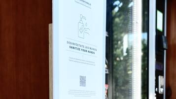 A hand sanitizer dispenser mounted on a wooden wall next to a window with a QR code and a sign.
