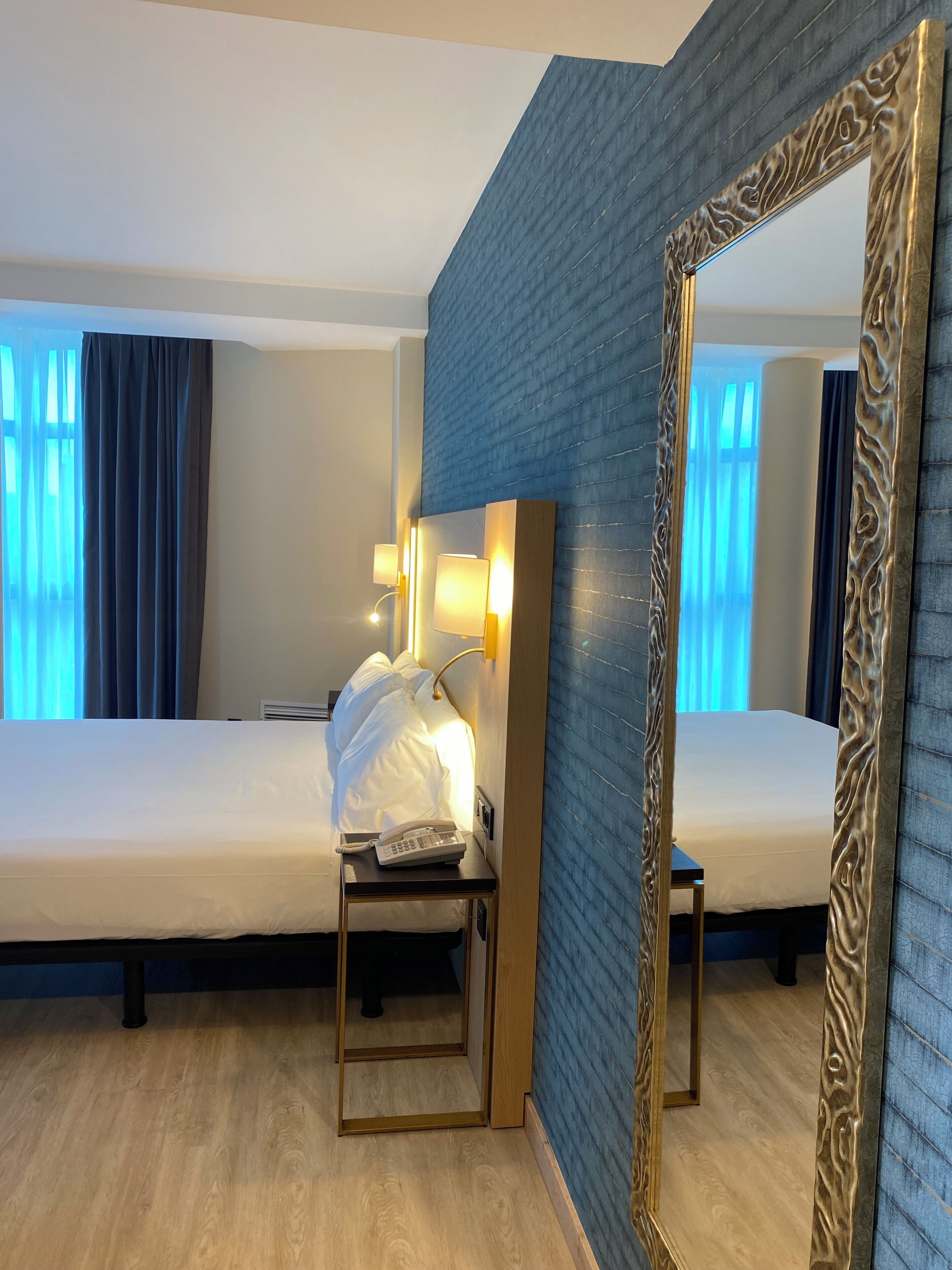 Une chambre d’hôtel avec deux lits, une table de chevet avec un téléphone et un miroir doté d’un cadre orné.