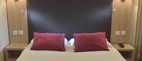 A hotel room with a large bed, two red pillows, bedside lamps, and a wooden headboard.