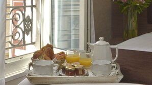 Bandeja de desayuno con cruasanes, zumo de naranja y café en un balcón con vistas a edificios.