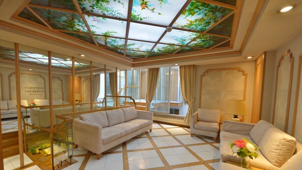 Una habitación amplia con techo de cristal, un sofá, una silla y una mesita con un florero.
