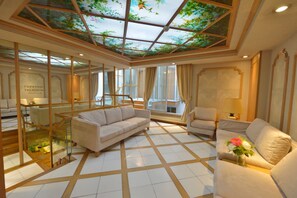A spacious room with a glass ceiling, a sofa, a chair, and a small table with a vase of flowers. - Hotel Renoir*** Paris Montparnasse (Paris)