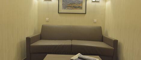 A room with a beige sofa, a wooden coffee table with a remote control, and two wall-mounted lamps.
