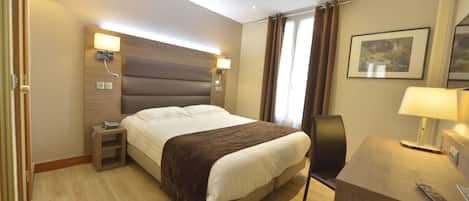 Habitación de hotel con una cama, mesitas de noche, un escritorio, una lámpara y un cuadro en la pared.