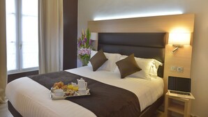 Habitación de hotel con una cama grande, una mesita de noche con lámpara y una bandeja con alimentos para el desayuno.