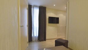 Habitación de hotel con piso de madera, televisor de pantalla plana en la pared, una mesita con control remoto y un sofá de color oscuro.