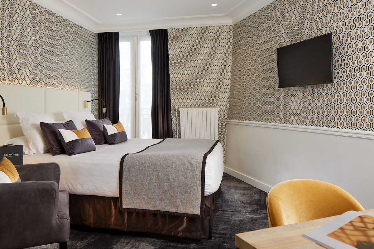 A hotel room with a bed, a desk, a chair, and a TV mounted on the wall.