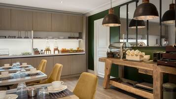Un espace repas moderne avec une table en bois dressée pour un repas, un coin café et une cuisine en arrière-plan.