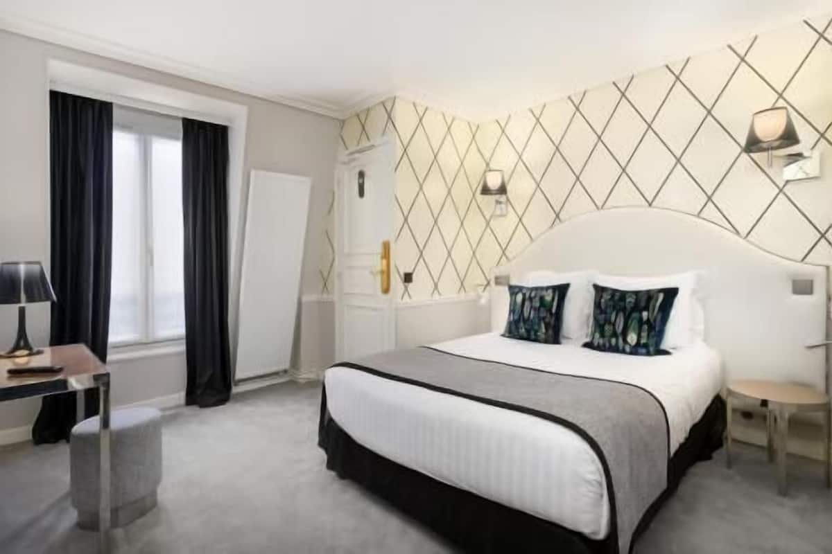 Ein Hotelzimmer mit Bett, Nachttisch, Lampe und einem fenster mit Vorhängen.