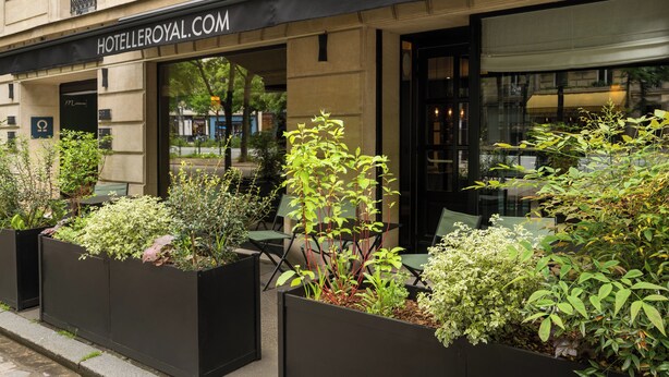 A hotel exterior with outdoor seating, planter boxes with plants, and a sign reading 'HOTELLEROYAL.COM'. - Hôtel Le Royal (Paris)