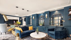 A modern living room with a blue sofa, a round coffee table, and a blue armchair. - Hôtel Le Royal (Paris)