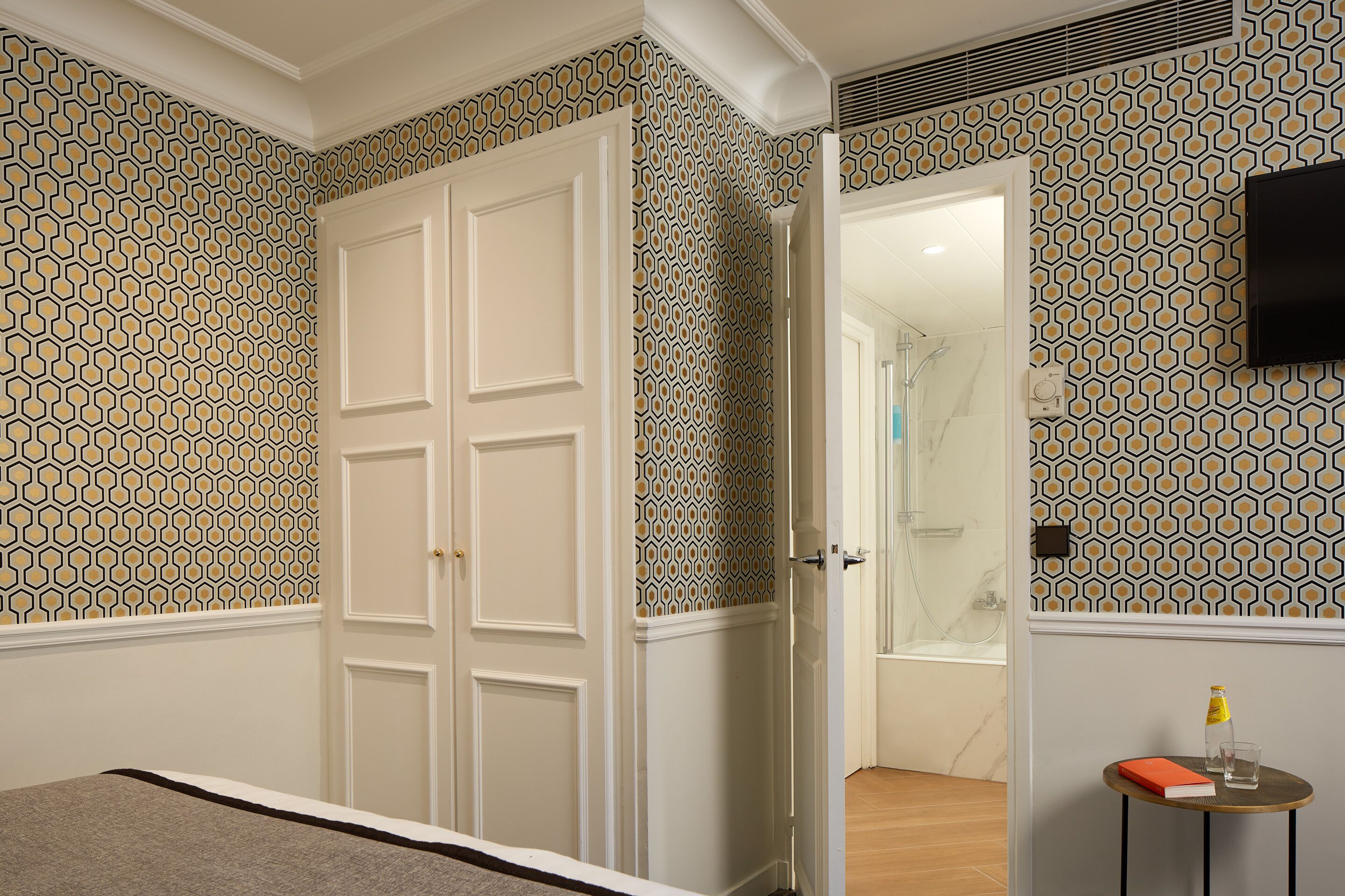 Ein Schlafzimmer mit Bett, Kleiderschrank, Badezimmer mit Dusche und einem kleinen Tisch mit Buch und Flasche.