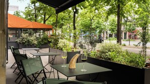 An outdoor seating area with tables and chairs, surrounded by greenery and a view of the street. - Hôtel Le Royal (Paris)