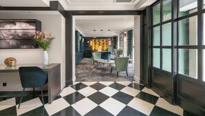A hotel lobby with a checkered floor, a reception desk, seating area, and a view through large windows. - Hôtel Le Royal (Paris)